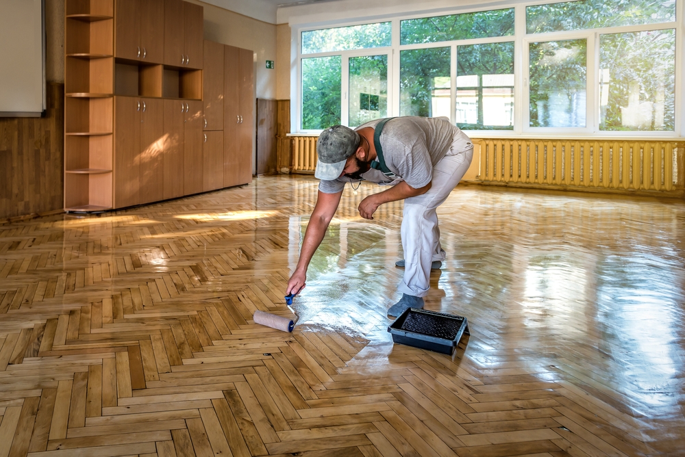 Painter rolling a clear sealer across a timber parquet floor in a Central Coast commercial space