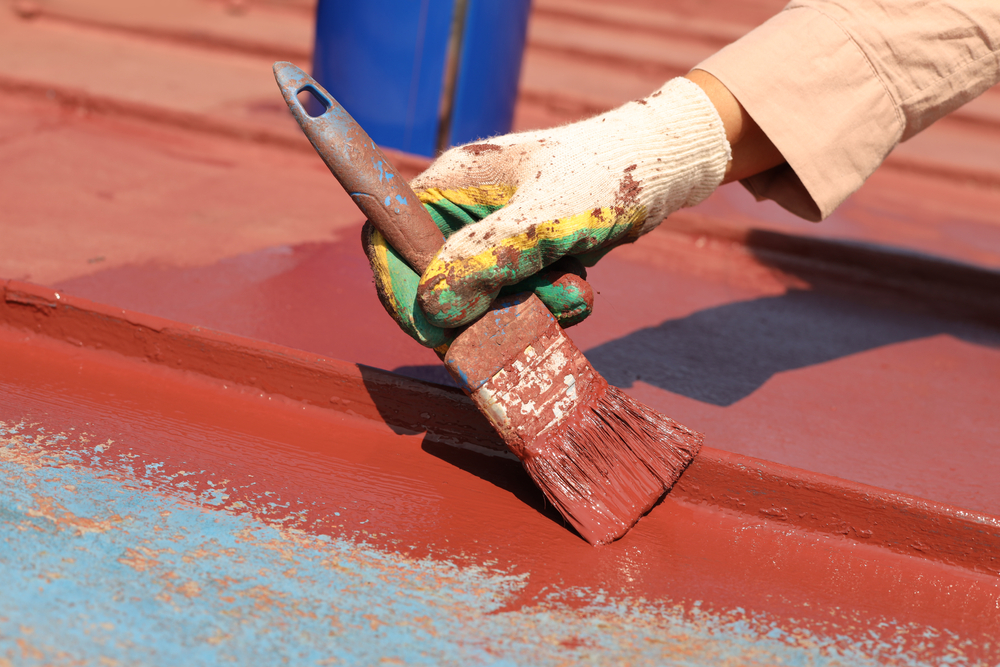Painter brushing fresh red protective coating onto a metal roof on a Maitland job