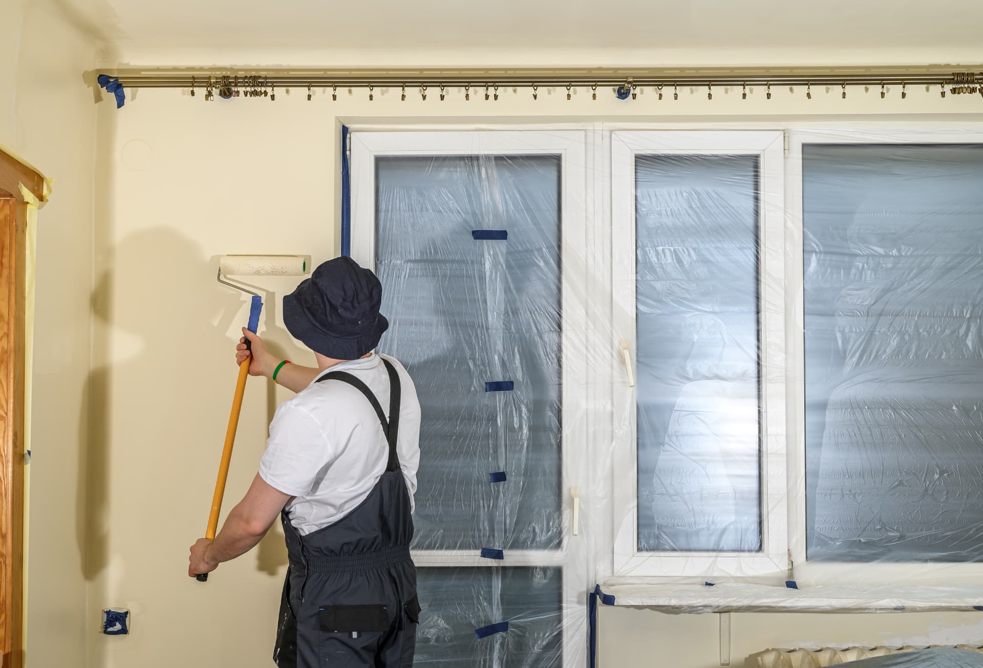 Painter rolling a fresh coat onto an interior wall beside masked windows in a Lake Macquarie home